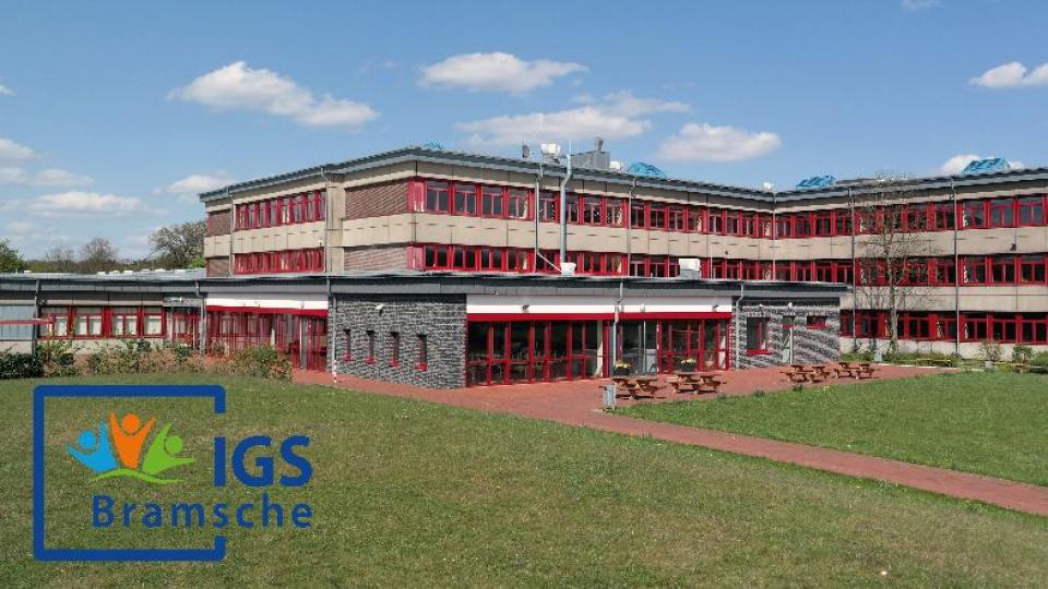 Schulgebäude der IGS Bramsche mit mehrstöckigem Bau und rotem Fassadenelement auf einer grünen Wiese unter blauem Himmel