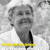 Person (Ilka Marlen Holtgrave) mit hellen, zerzausten Haaren und weißem Hemd vor unscharfem Pflanzenhintergrund