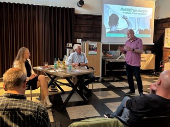 Ein Bürger gibt ein Statemant für den Lütti in Bramsche ab. Neben ihm am Tisch sitzen Landrätin Anna Kebschull und Bürgermeister Heiner Pahlmann und hören gespannt zu. Im Vordergrund sind weitere Zuhörer im Publikum zu sehen. 