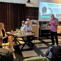 Ein Bürger gibt ein Statemant für den Lütti in Bramsche ab. Neben ihm am Tisch sitzen Landrätin Anna Kebschull und Bürgermeister Heiner Pahlmann und hören gespannt zu. Im Vordergrund sind weitere Zuhörer im Publikum zu sehen. 