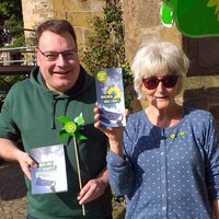 Zwei Personen halten Flyer und ein kleines grünes Windrad in die Kamera