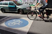 Fahrradfahrer auf Straße mit blauem Fahrradsymbol und parkendem Auto vor einer mit Graffiti besprühten Wand