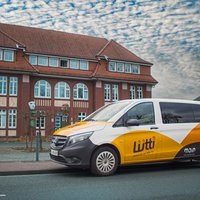 Gelb-weißer Van mit der Aufschrift »Lütti« steht vor dem historischen Rathaus in Bramsche unter bewölktem Himmel