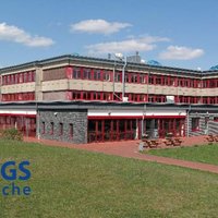 Schulgebäude der IGS Bramsche mit mehrstöckigem Bau und rotem Fassadenelement auf einer grünen Wiese unter blauem Himmel