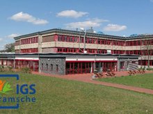 Schulgebäude der IGS Bramsche mit mehrstöckigem Bau und rotem Fassadenelement auf einer grünen Wiese unter blauem Himmel