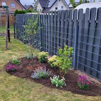 Neu angelegtes Beet mit verschiedenen kleinen Sträuchern und Blumen vor einem grauen Zaun in einem Garten